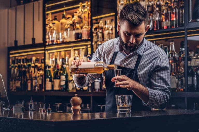 Stylish bartender in a shirt and apron standing at bar counter background