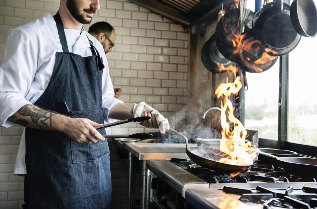 Professional cook making food in a pan with flames at a restaurant.